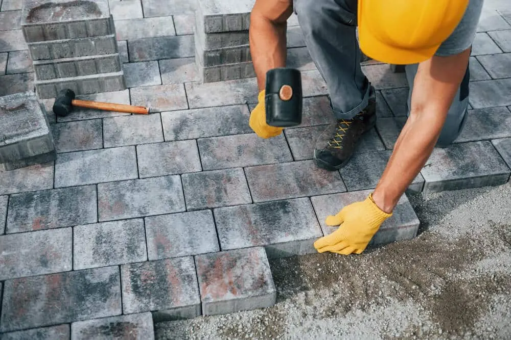 Worker in a hard hat setting gray paving stones with a rubber mallet