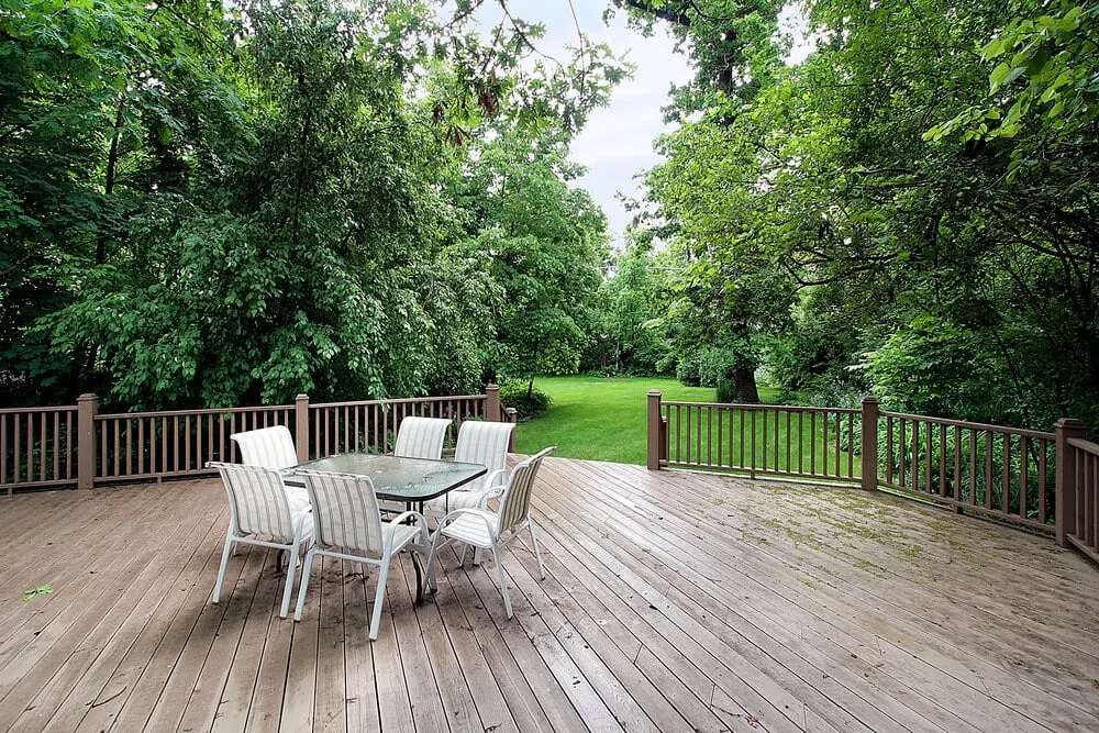 Wooden deck with a white patio table and chairs overlooking a wooded lawn