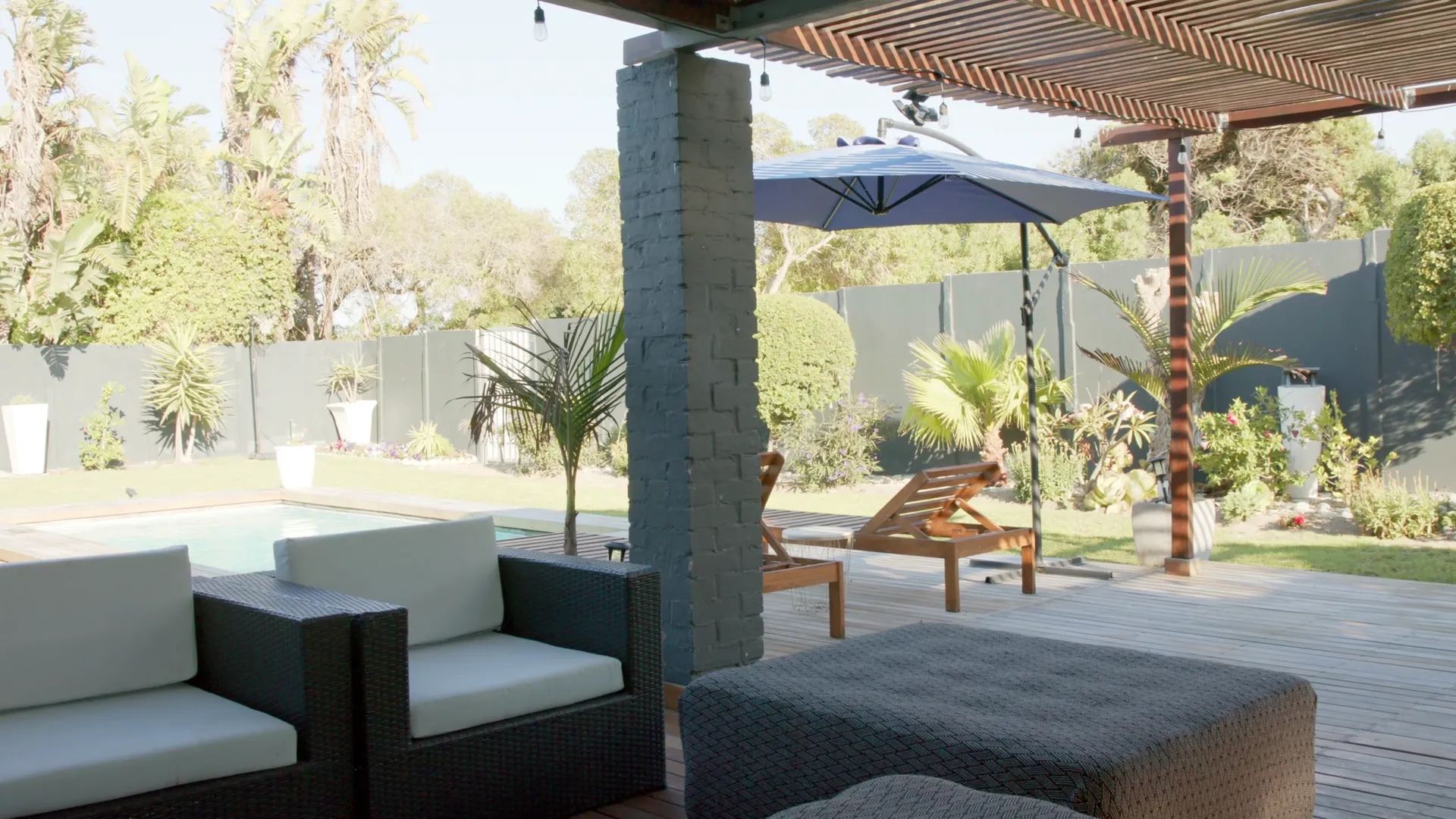 Covered patio with wicker lounge seating, a shade umbrella and deck loungers