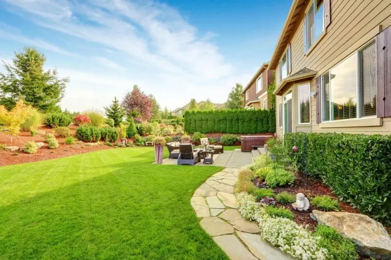 Backyard lawn with a stone path, patio furniture, and planted borders