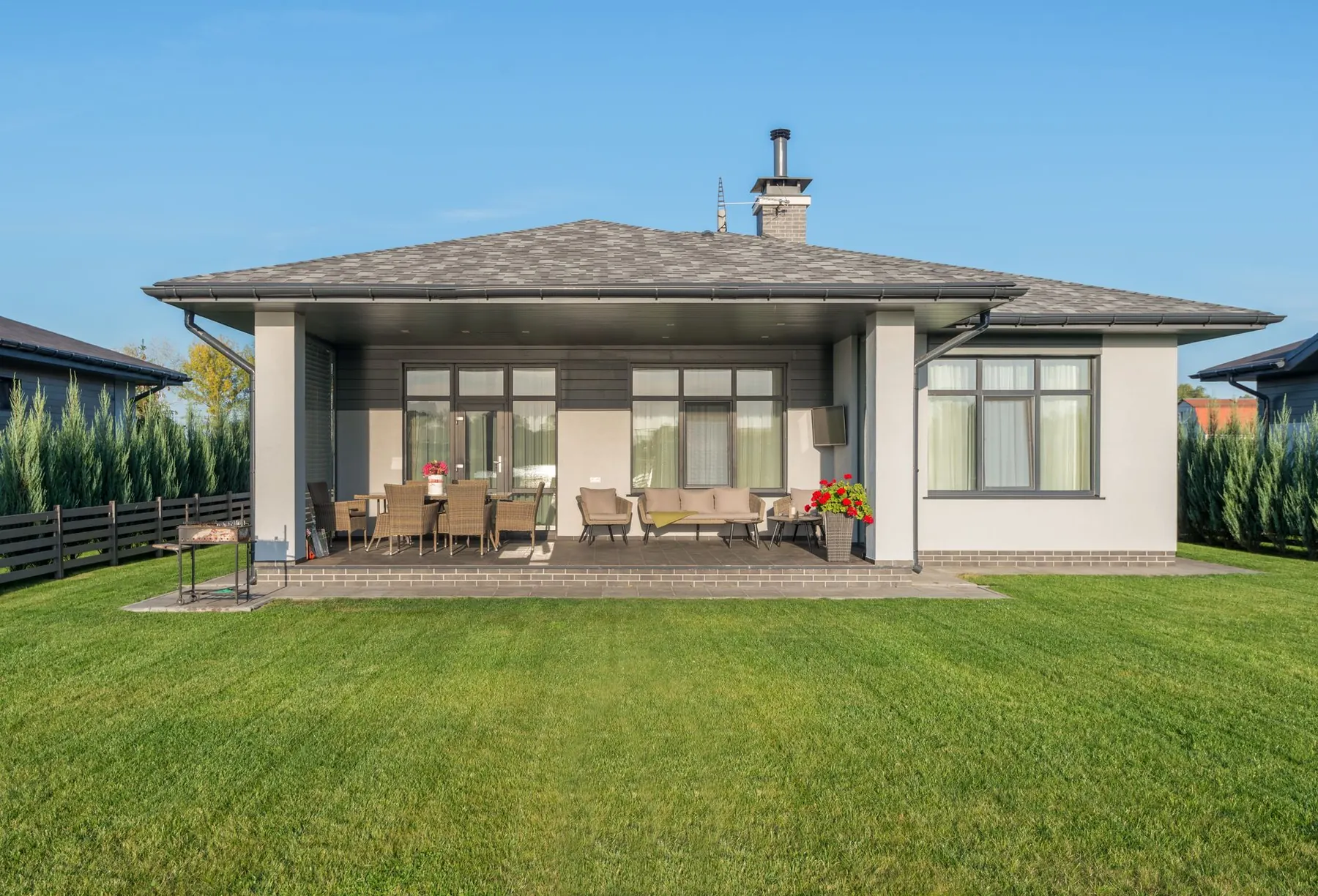 Single-story home with outdoor dining and lounge furniture on a covered patio behind a wide lawn
